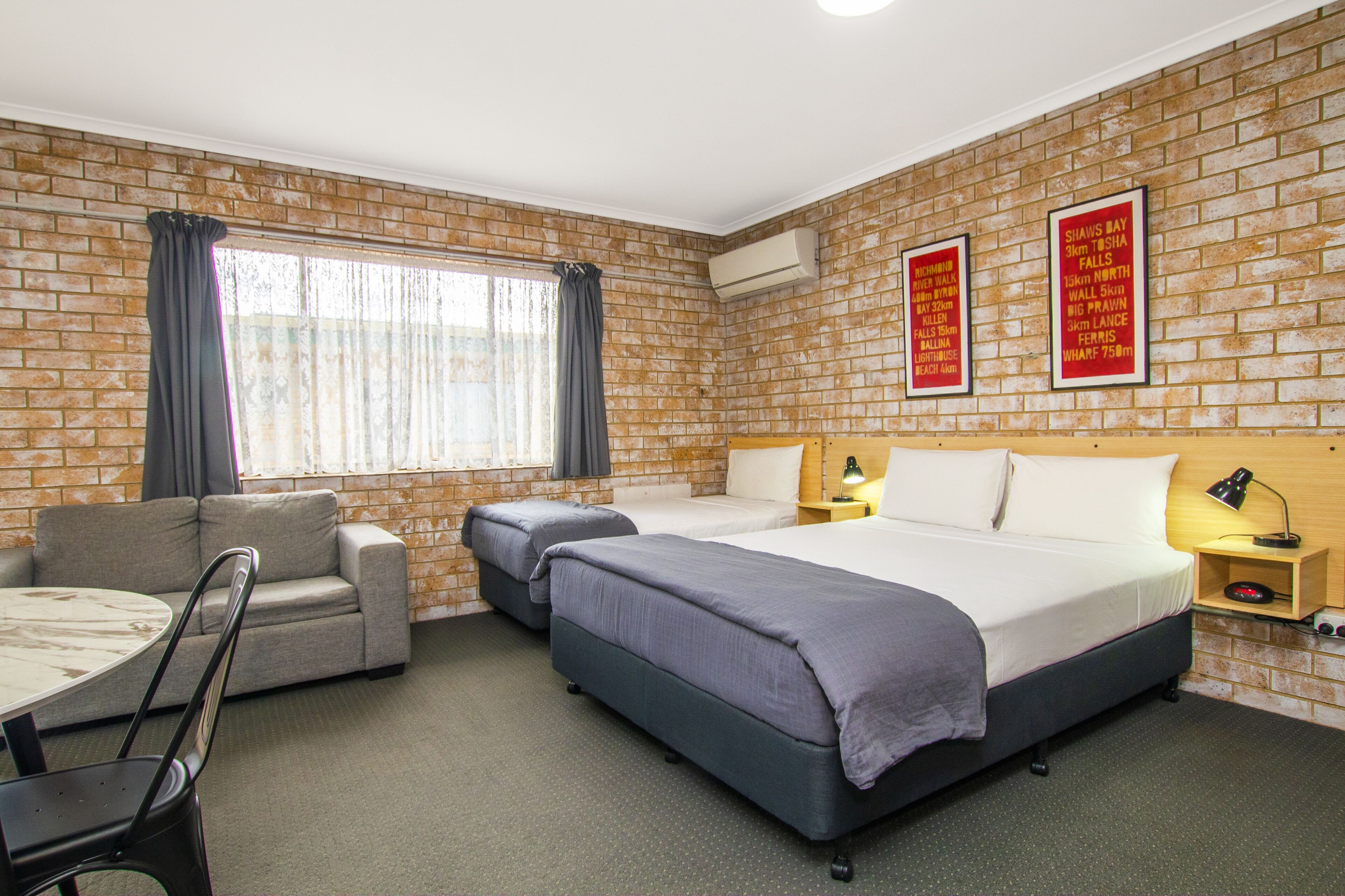 A hotel room with a brick wall, two beds, a sofa, a table, and a chair.