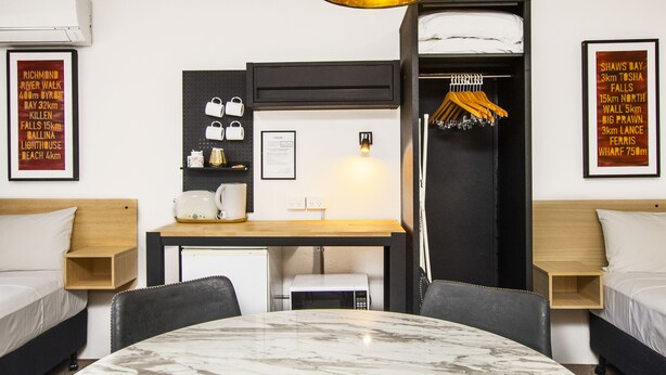 Habitación de hotel con cama, escritorio, silla, mesa, microondas, lámpara colgante y armario.
