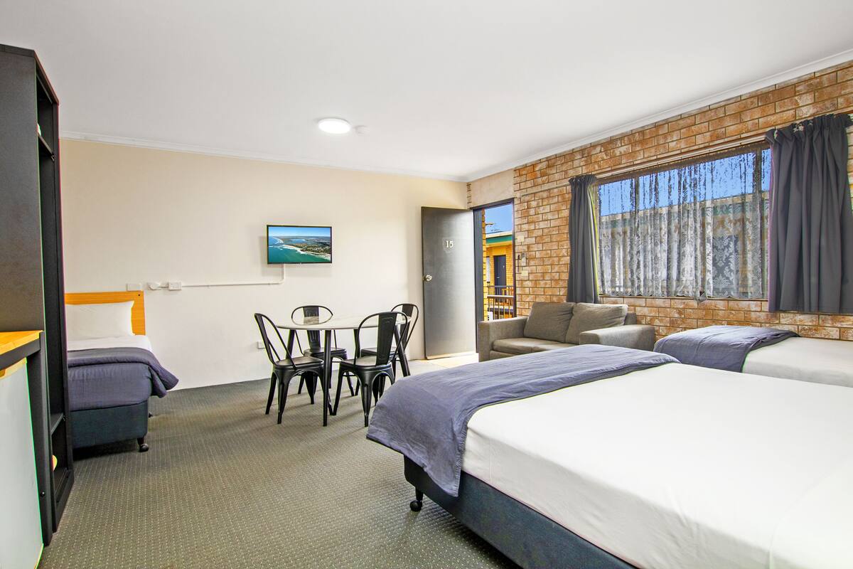 A hotel room with two beds, a dining table, chairs, a TV, and a brick wall.