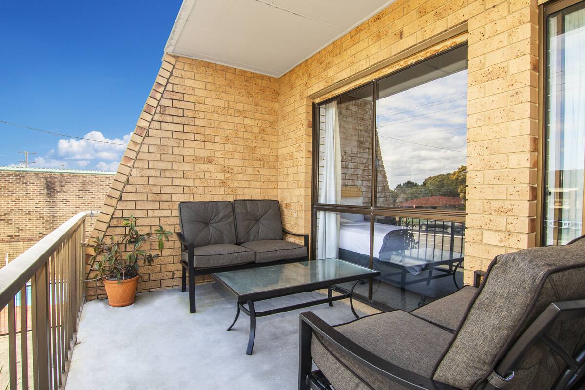 A balcony with a brick wall, a glass table, two sofas, and a potted plant.