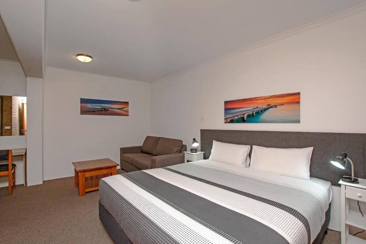 A hotel room with a bed, a desk, a chair, and two paintings on the wall.