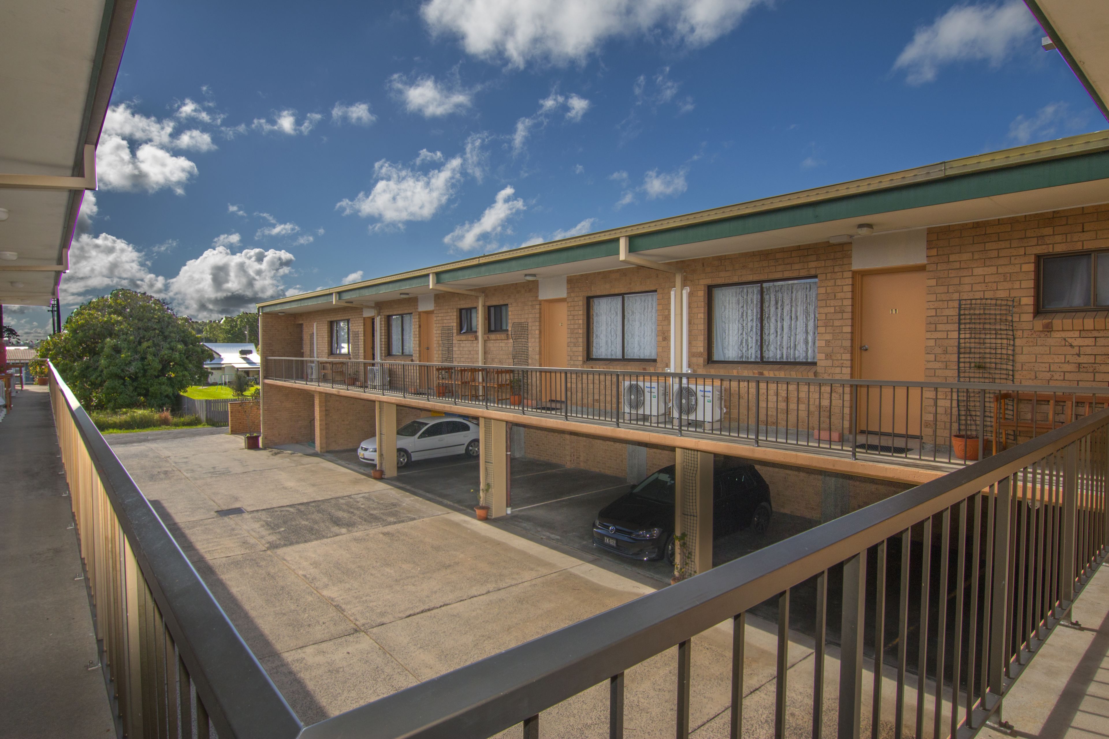 A motel with a covered parking area, multiple rooms, and a balcony.