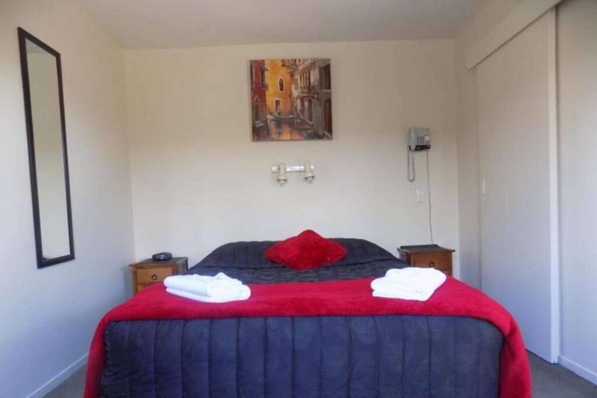 Une chambre à coucher avec un lit, un oreiller rouge, deux tables de chevet, un tableau accroché au mur et un téléphone.