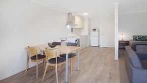 Een moderne keuken met witte kasten, een magnetron en een ingebouwde oven. Er is een eethoek met een houten tafel en stoelen.