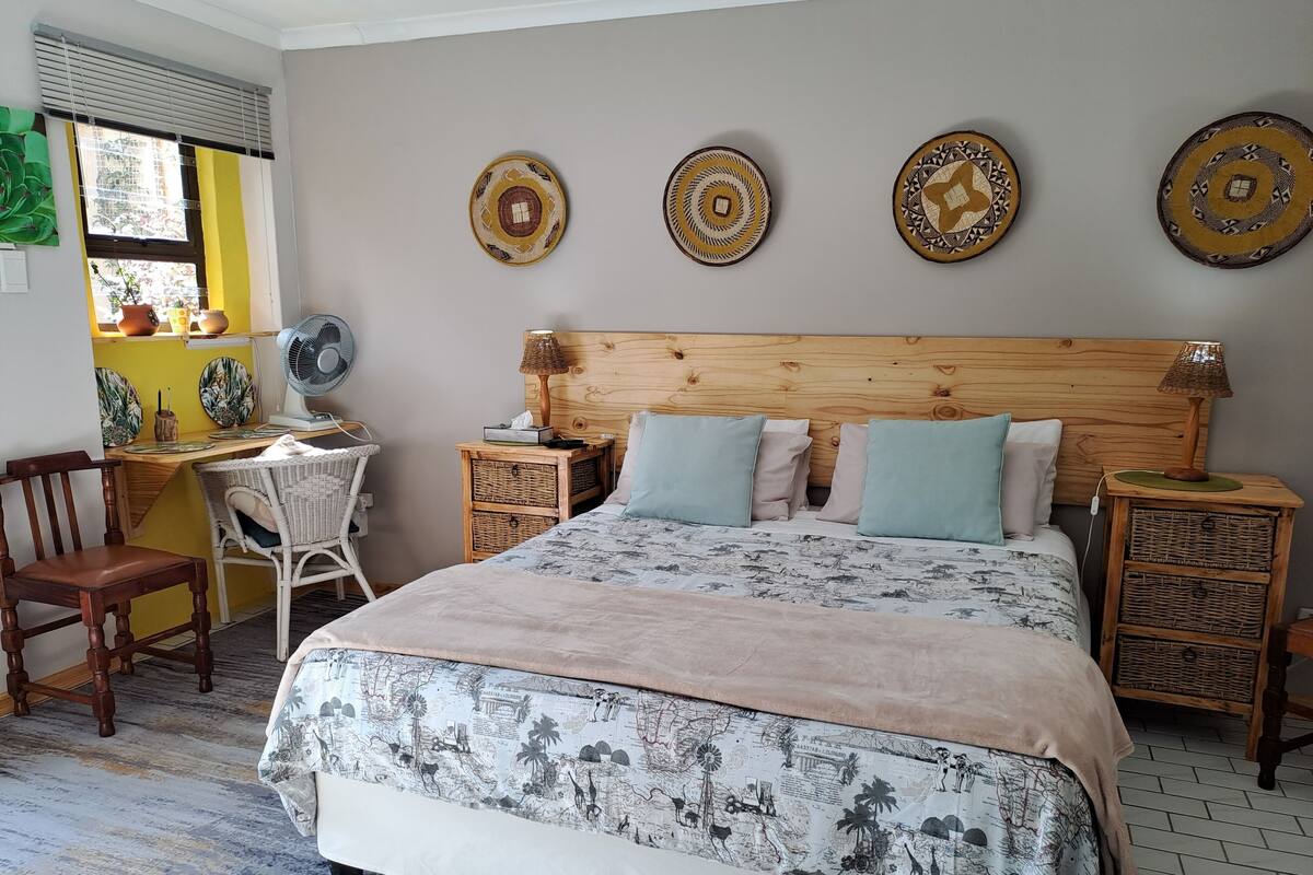 A bedroom with a wooden headboard, a bed with patterned bedding, a desk with a chair, and decorative plates on the wall.