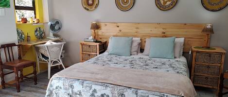 A bedroom with a wooden headboard, a bed with patterned bedding, a desk with a chair, and decorative plates on the wall.