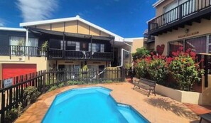 A residential building with a swimming pool, a fenced area, and a bench.