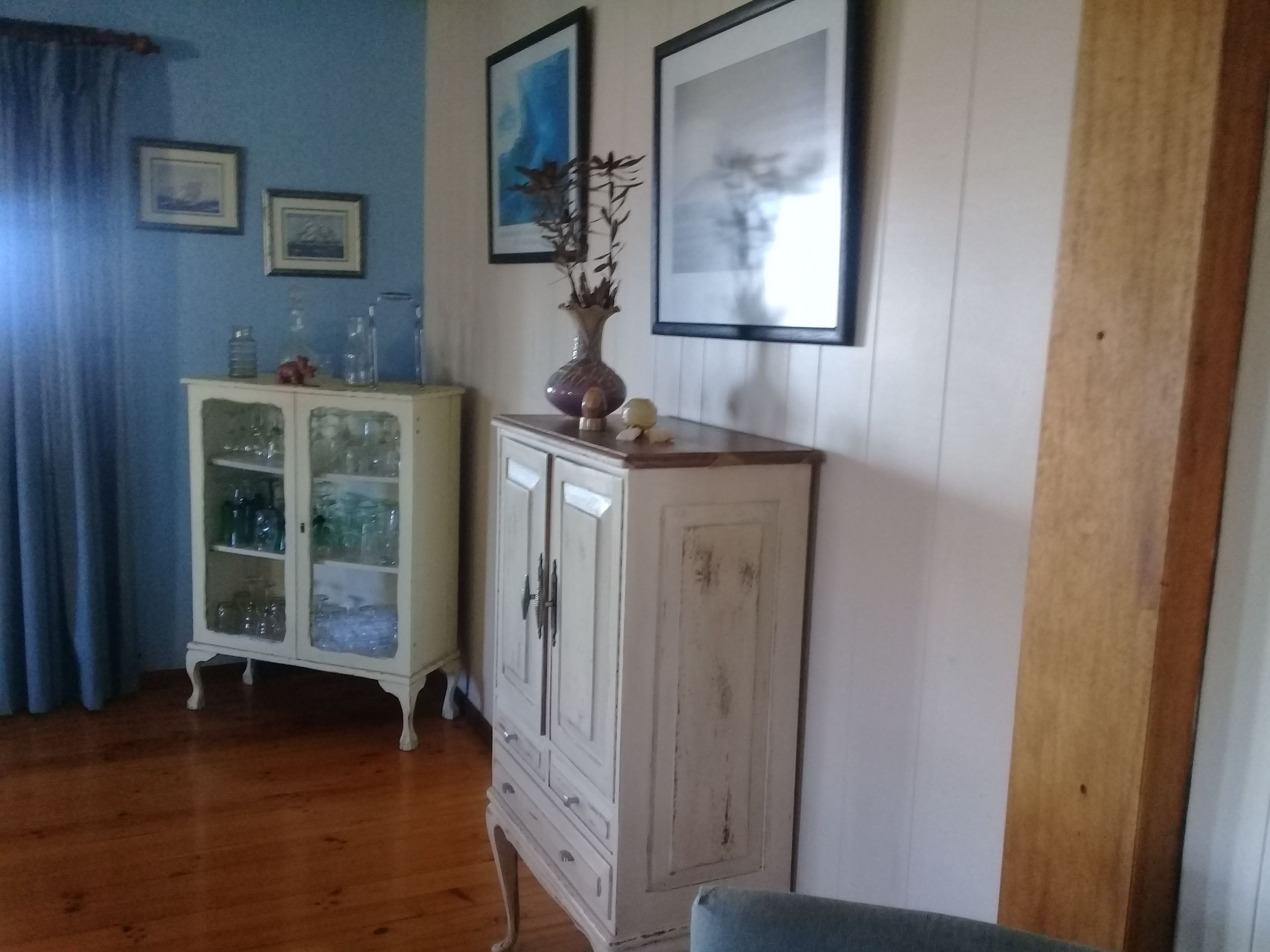 Una habitación con piso de madera, un armario blanco con puertas de vidrio y una silla azul.