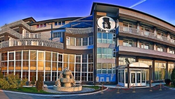 A modern hotel with a curved facade, large windows, and a central entrance with a turnstile.
