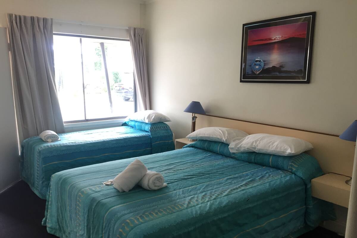 Ein Hotelzimmer mit zwei Betten, einem Fenster mit Vorhängen, einem Nachttisch mit Lampe und einem gerahmten Bild an der Wand.