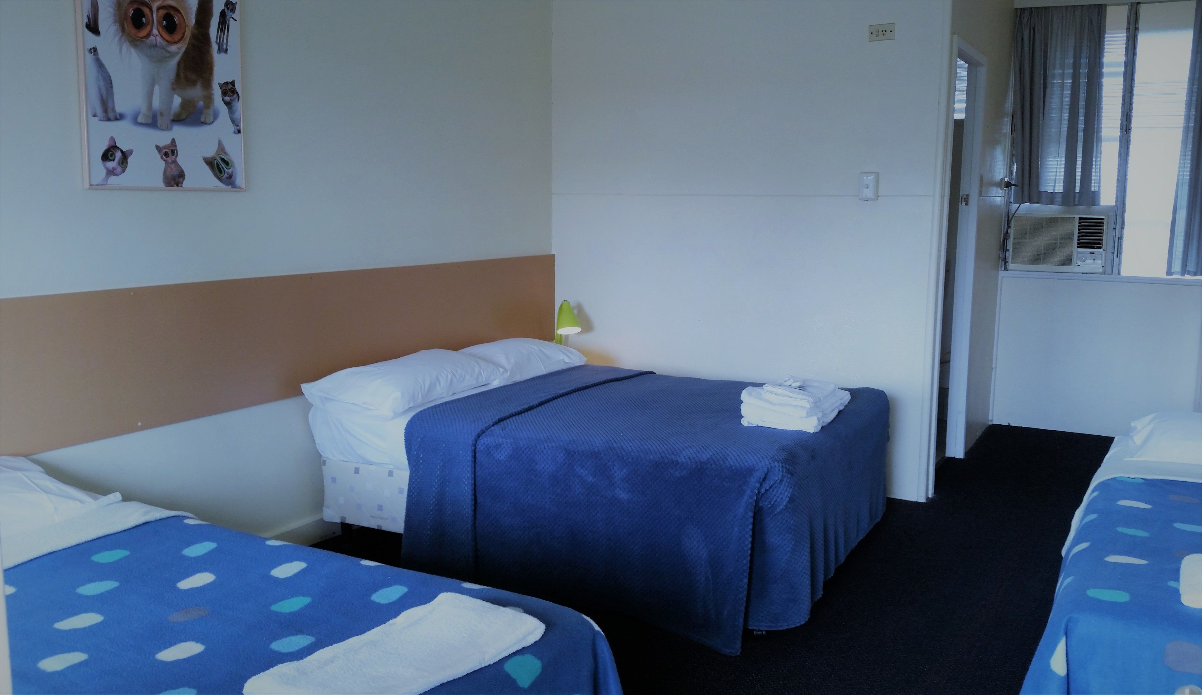 A hotel room with two beds, a wall-mounted air conditioner, and a window with curtains.