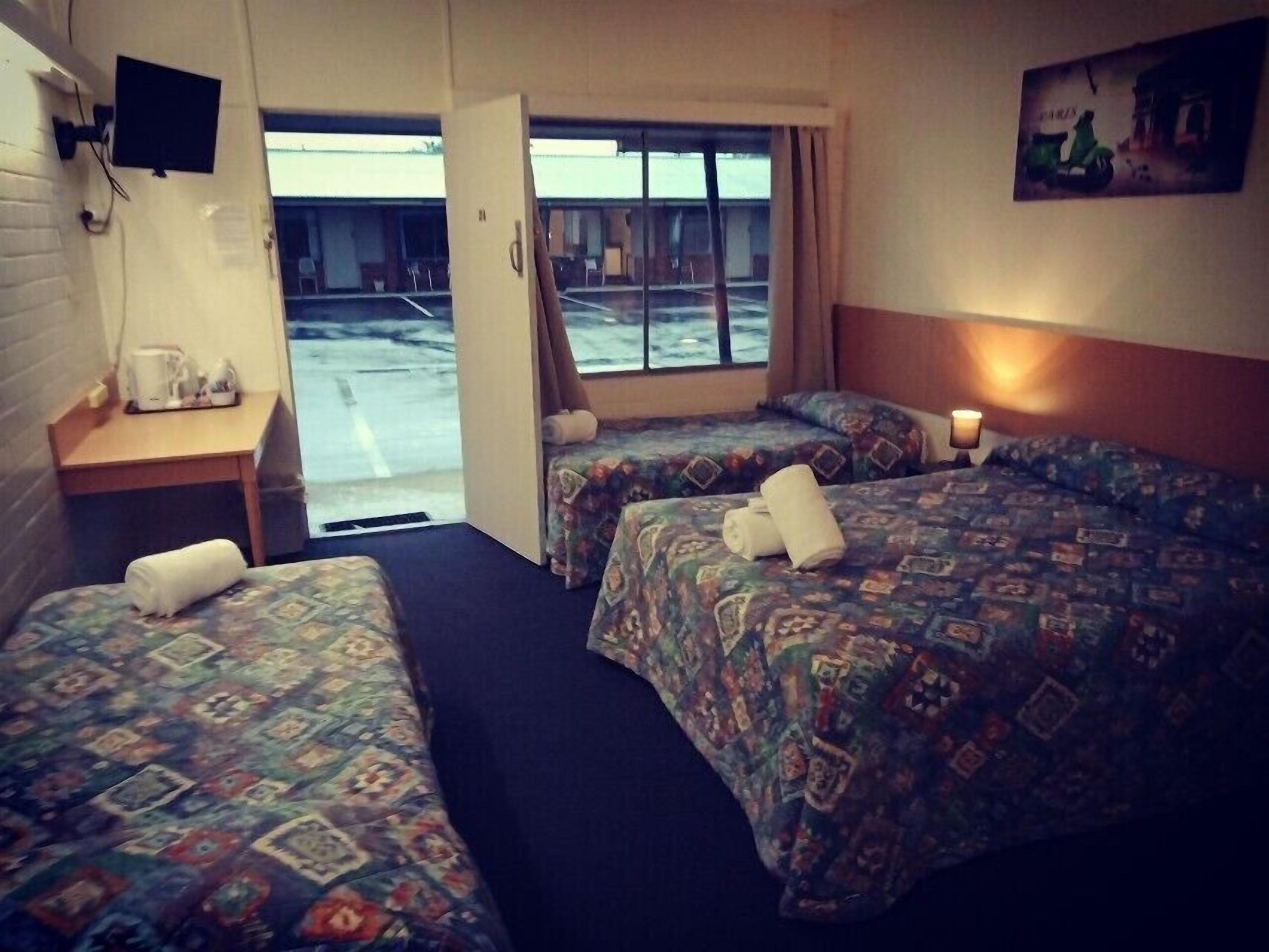 A hotel room with two beds, a small table with a coffee maker, and a TV mounted on the wall.
