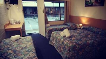 A hotel room with two beds, a small table with a coffee maker, and a TV mounted on the wall.