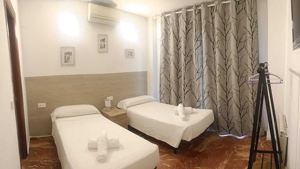 A hotel room with two single beds, a wooden headboard, a marble floor, a radiator, and a curtain with a tree pattern. - Hostal Nevot (Granada)