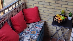 A blue sofa with red cushions against a brick wall, a small table with a fruit basket, and a potted plant. - Hostal Nevot (Granada)