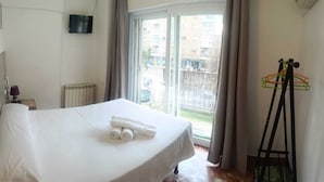 A hotel room with a bed, a TV on the wall, a radiator, and a view of the outside. - Hostal Nevot (Granada)
