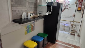 A kitchenette with a microwave, a black refrigerator, and a shelf with cups and a box of tissues. There are three trash bins in yellow, blue, and green. - Hostal Nevot (Granada)
