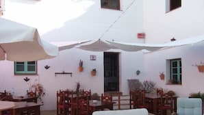 A covered outdoor seating area with tables and chairs, potted plants, and a white wall. - Hotel Palacete de Mañara (Montejaque)