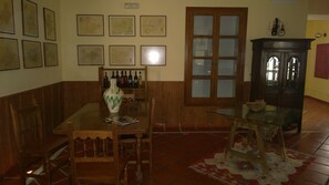 A dining area with a wooden table, chairs, a vase, and framed maps on the wall. - Hotel Palacete de Mañara (Montejaque)