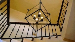 A staircase with a geometric metal railing and a hanging light fixture with three bulbs. - Hotel Palacete de Mañara (Montejaque)