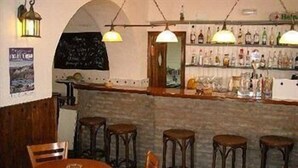 A bar area with wooden stools, hanging lamps, and shelves of bottles. - Hotel Palacete de Mañara (Montejaque)