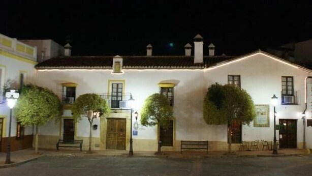 A white building with a tiled roof, multiple windows, and a small porch area with a bench. - Hotel Palacete de Mañara (Montejaque)