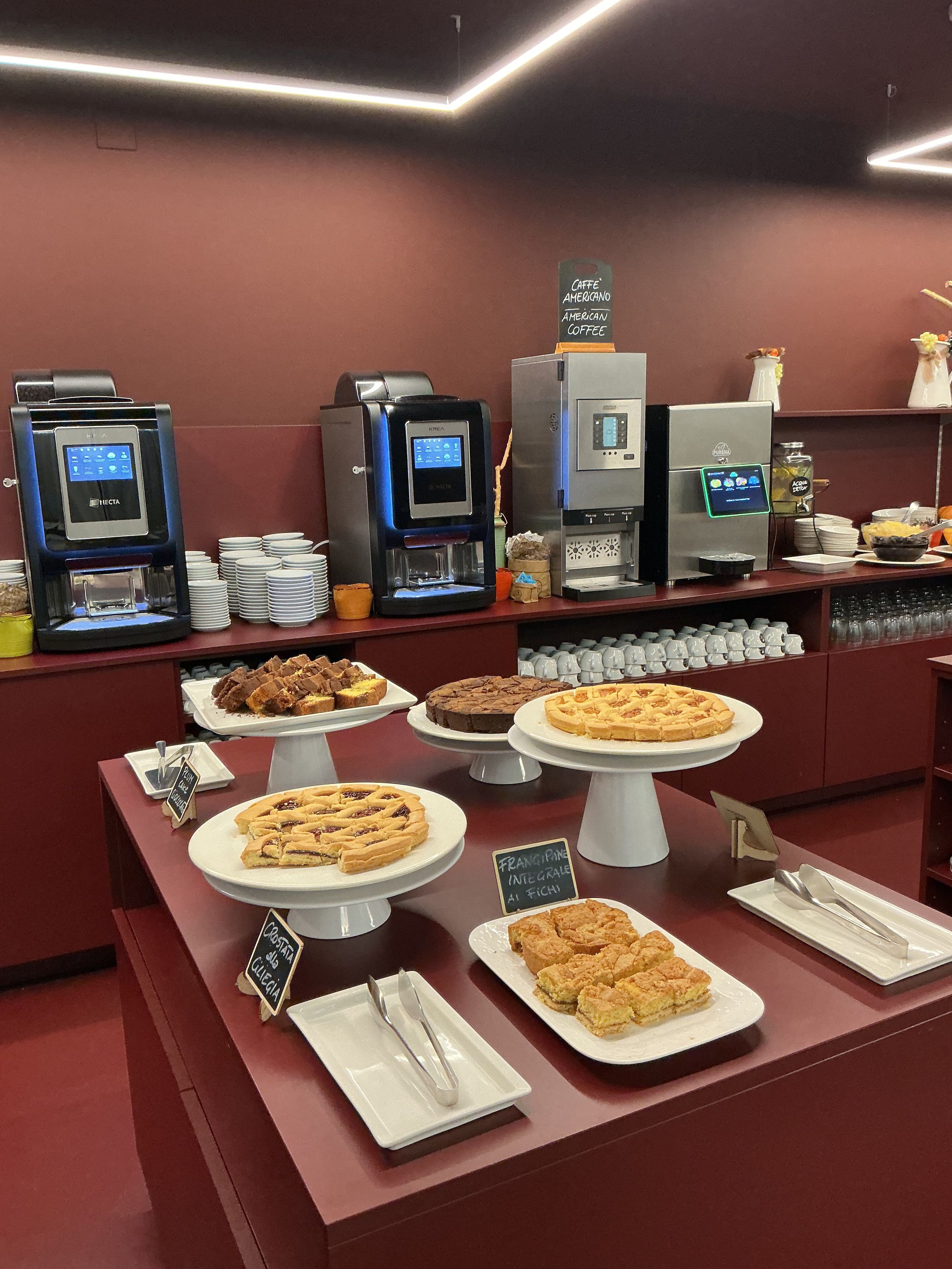 A coffee station with multiple espresso machines and a variety of pastries displayed on white stands.