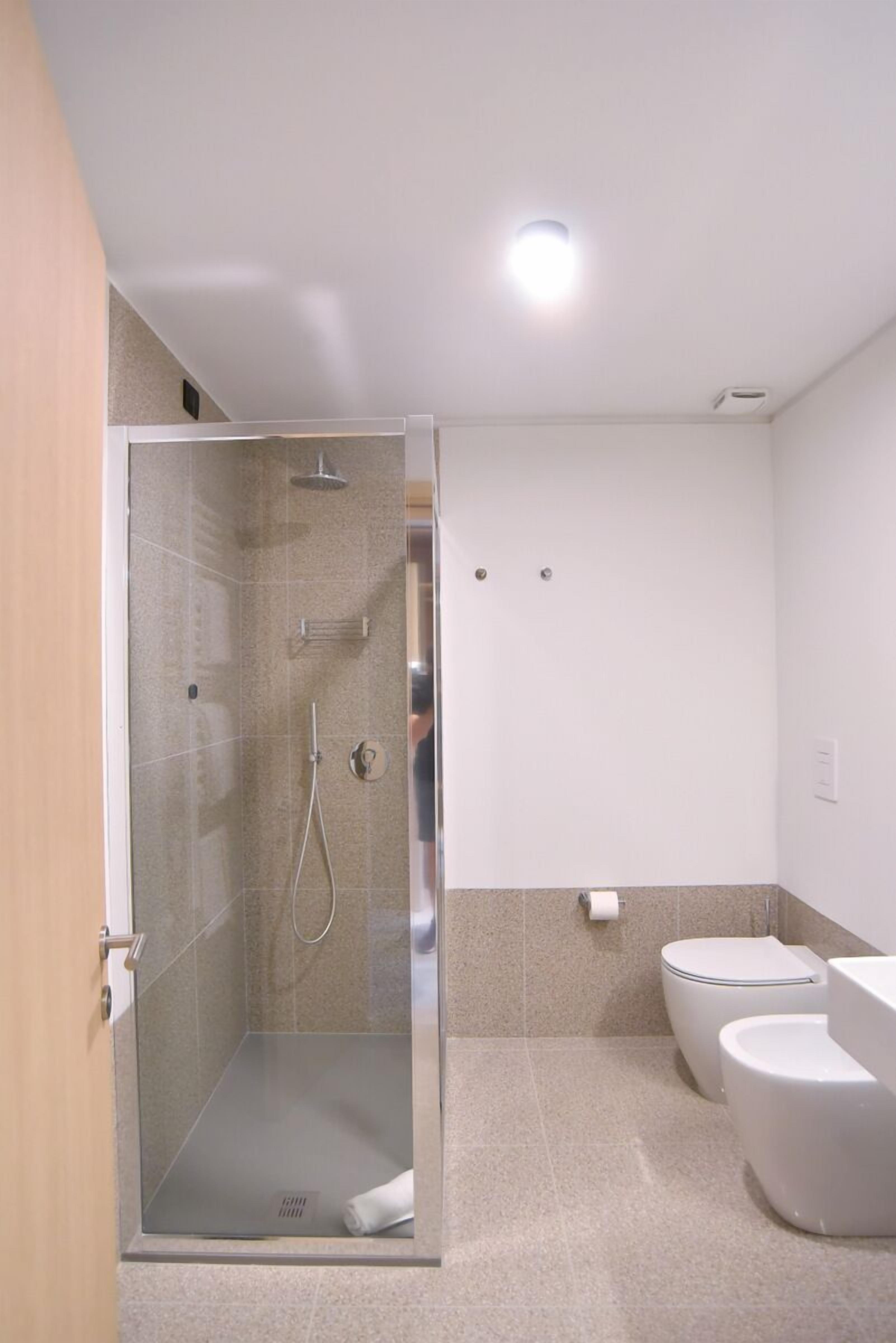A modern bathroom with a glass-enclosed shower, two toilets, and a visible toilet paper dispenser.
