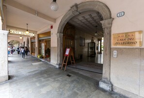 A hotel entrance with a stone facade, a sign for 'Hotel Casa del Pellegrino', and a cafe in the background.