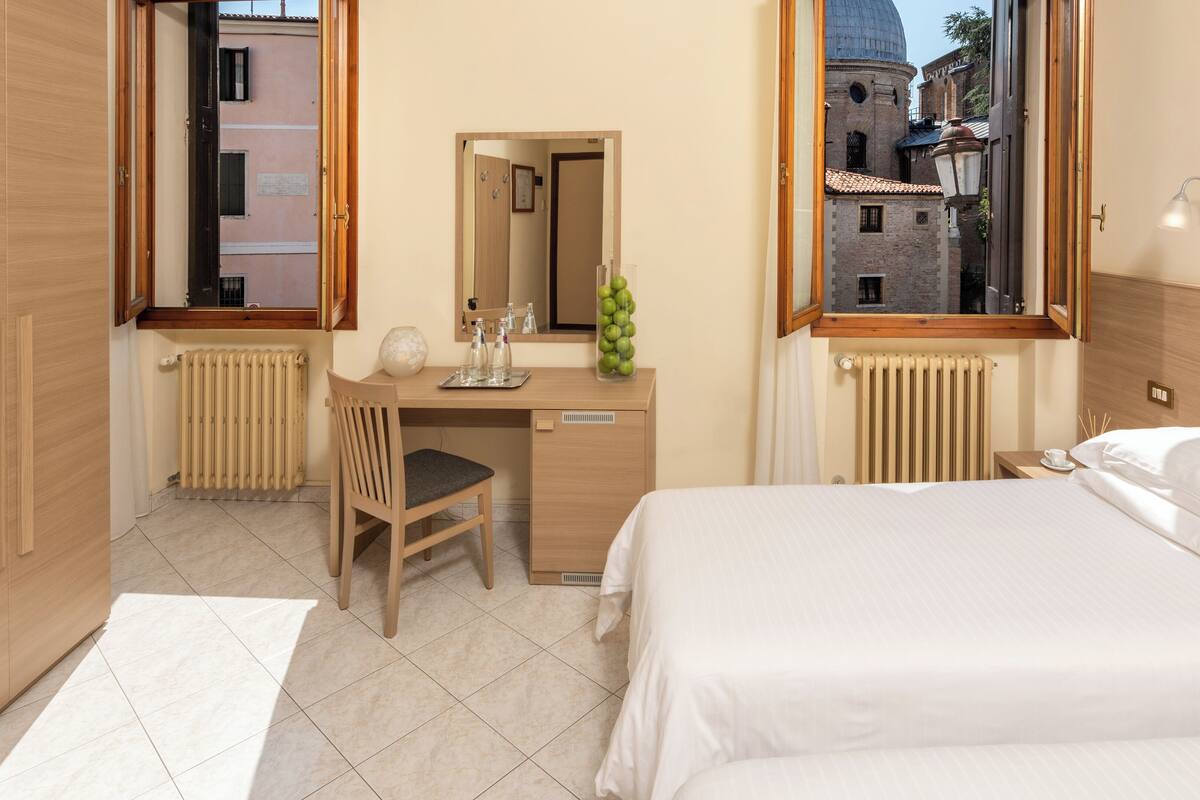 Habitación de hotel con cama, escritorio, silla, espejo y vista a un edificio a través de la ventana.