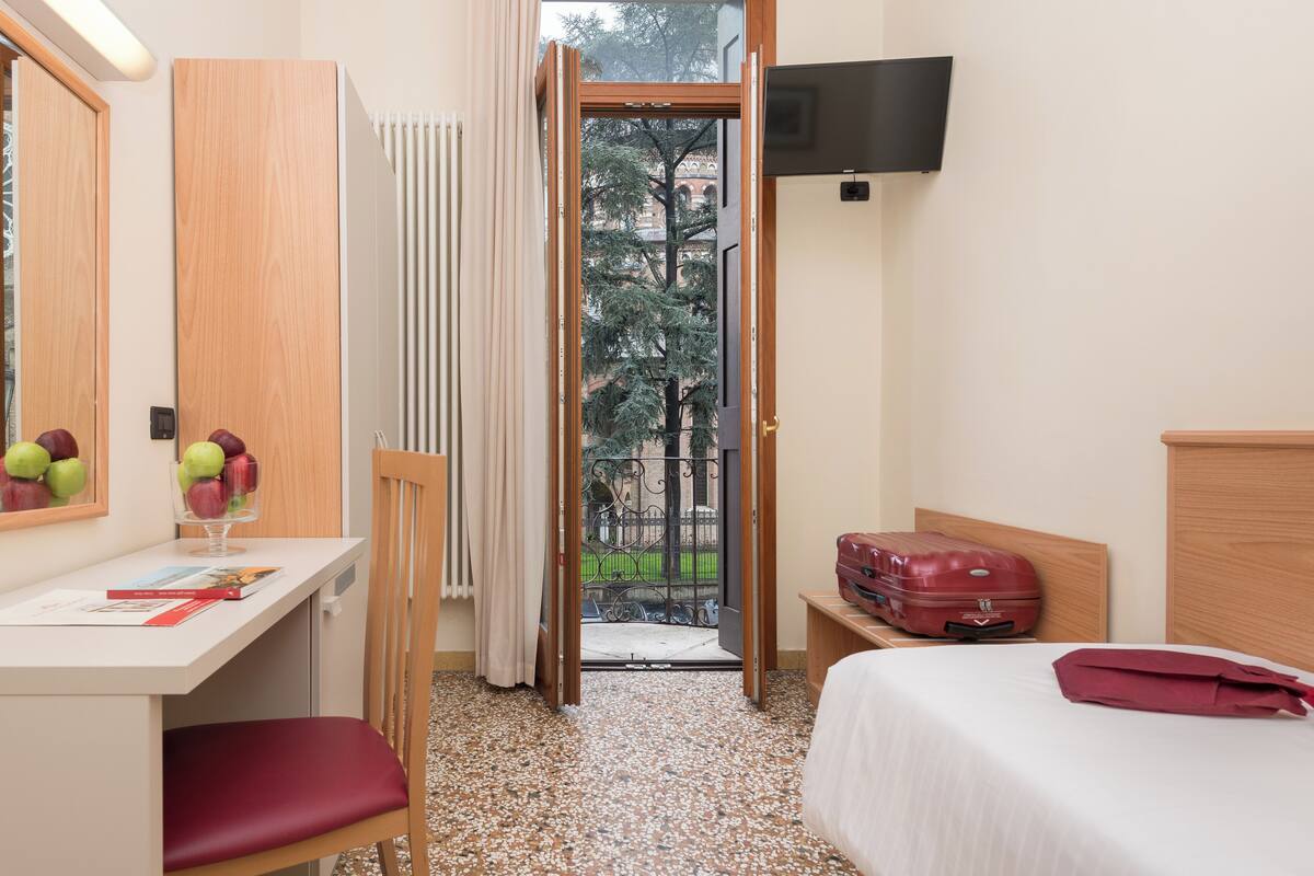 Habitación de hotel con cama, escritorio con silla, televisor en la pared y una maleta sobre la cama.