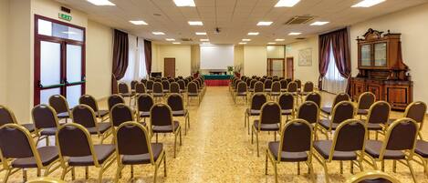 A conference room with rows of chairs, a podium, and a large window with curtains.