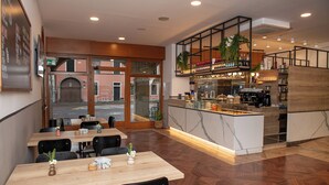 Een restaurant met houten tafels en stoelen, een bar met flessen op de planken, en uitzicht op de straat.