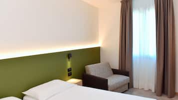 A hotel room with a green accent wall, a bed, a chair, a nightstand, and a window with curtains.
