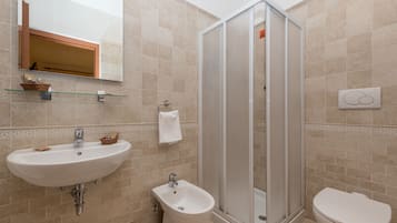 A bathroom with a sink, bidet, toilet, and a glass-enclosed shower.
