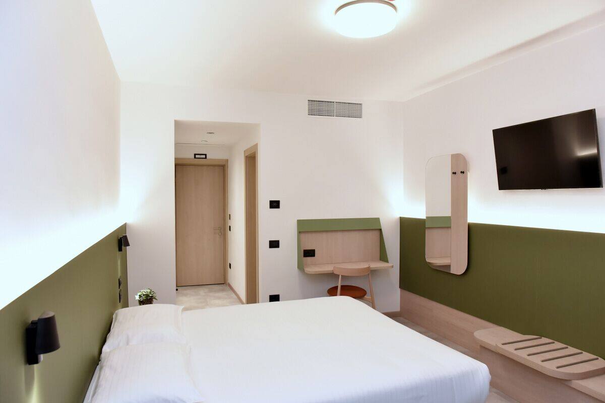 Habitación de hotel con una cama, un escritorio pequeño, un espejo y un televisor montado en la pared.