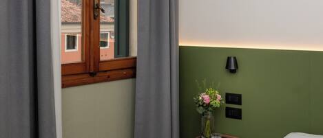 A hotel room with a view of a historic building through a window with wooden frames and grey curtains.