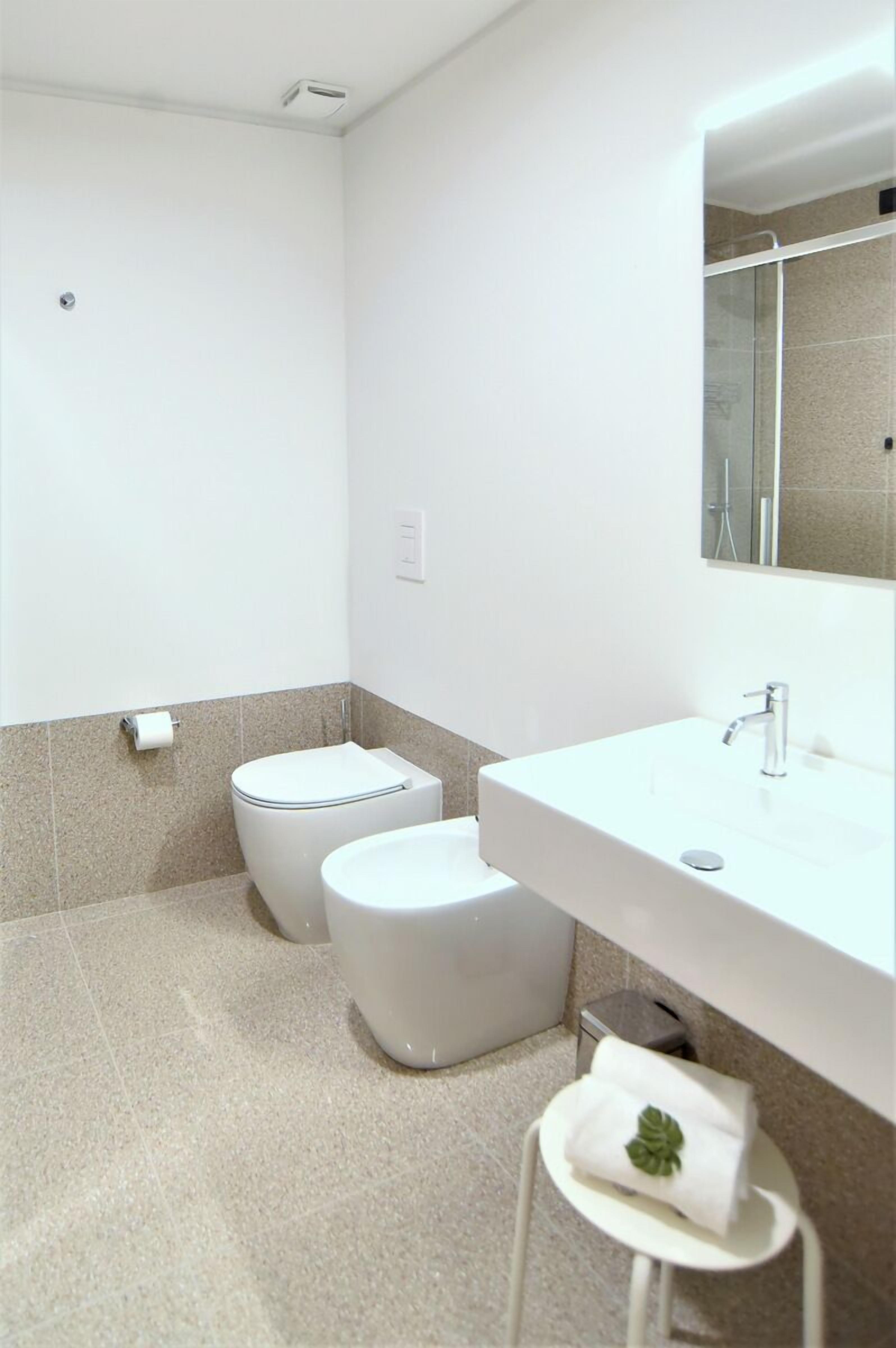 A modern bathroom with a white sink, a toilet, and a shower area.
