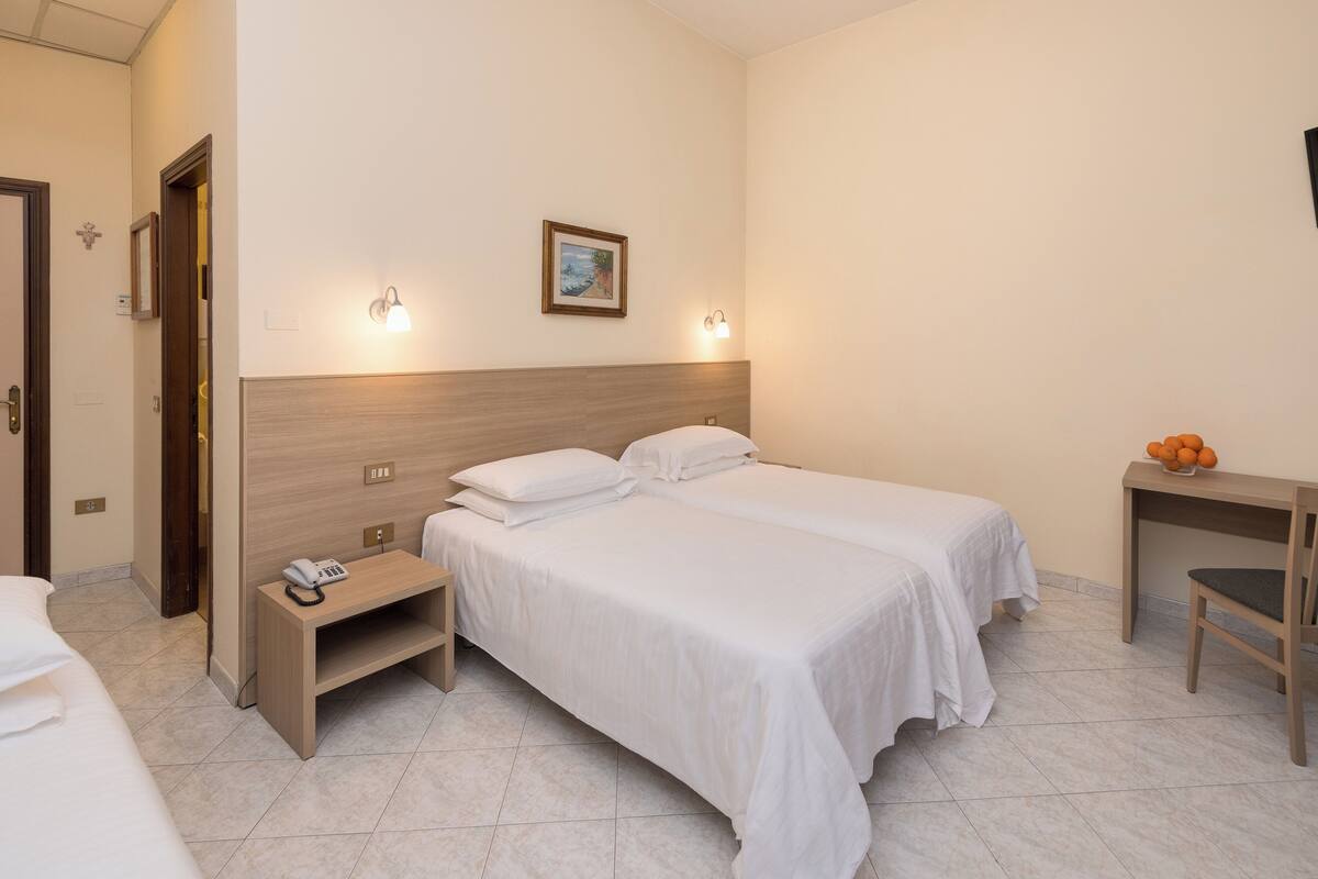 Habitación de hotel con dos camas, un escritorio, una silla, un teléfono y un televisor montado en la pared.