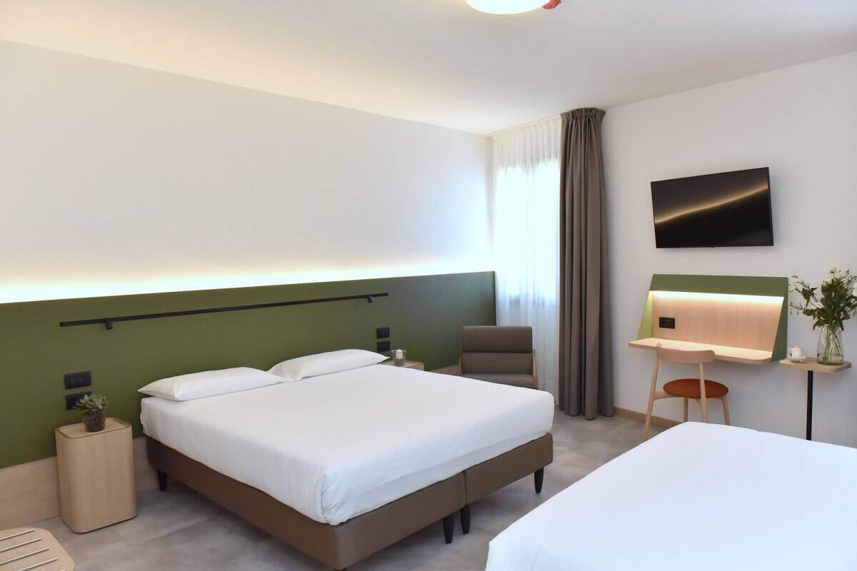 Habitación de hotel moderna con una cama grande, un escritorio con una silla, un televisor montado en la pared y una planta pequeña en la mesita de noche.