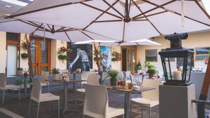 Een buiten eethoek met tafels, stoelen, parasols en plantenpotten.