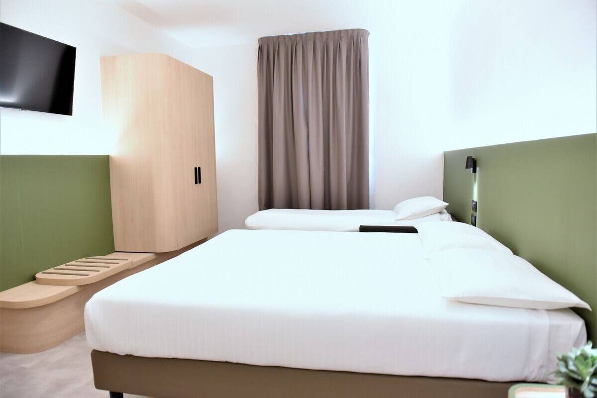 Una habitación de hotel con una cama, un armario, un televisor y una cortina.