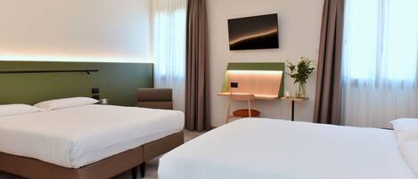A hotel room with two beds, a desk, a flat-screen TV, and a small plant.