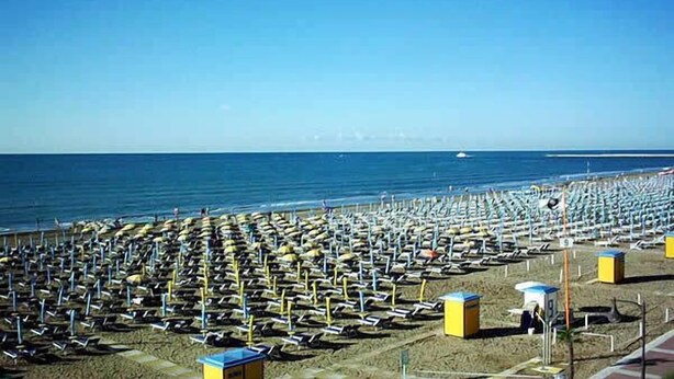 A beach with rows of sun loungers and umbrellas, a clear sky, and a calm sea. - Hotel Antonella (Caorle)