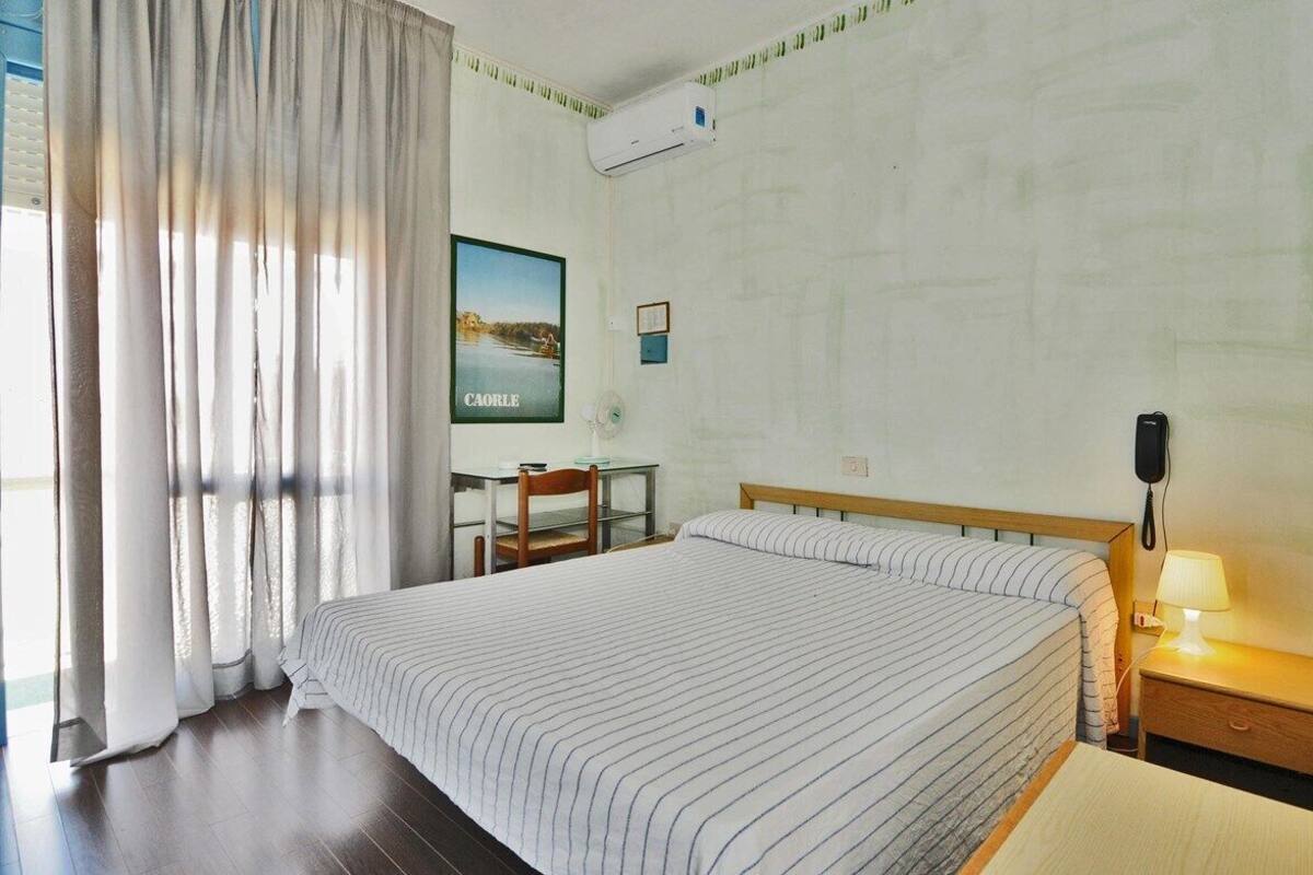Habitación de hotel con una cama grande, un escritorio, una silla, una mesita de noche con lámpara y un equipo de aire acondicionado en la pared.