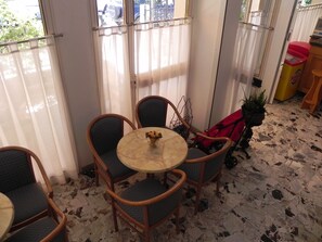 A small, sunlit room with a round table and four chairs, a potted plant, and a red stroller. - Hotel Antonella (Caorle)