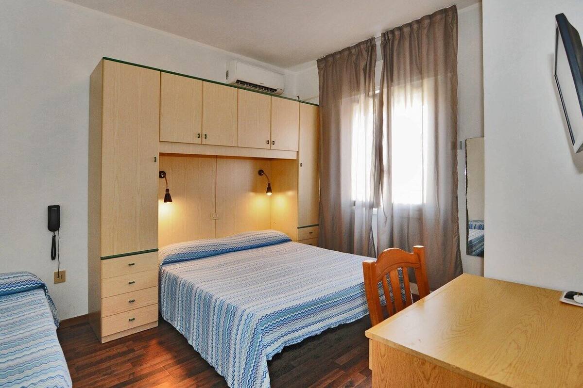Una habitación con dos camas, una mesa de madera, una silla, un armario, un teléfono y una ventana con cortinas.