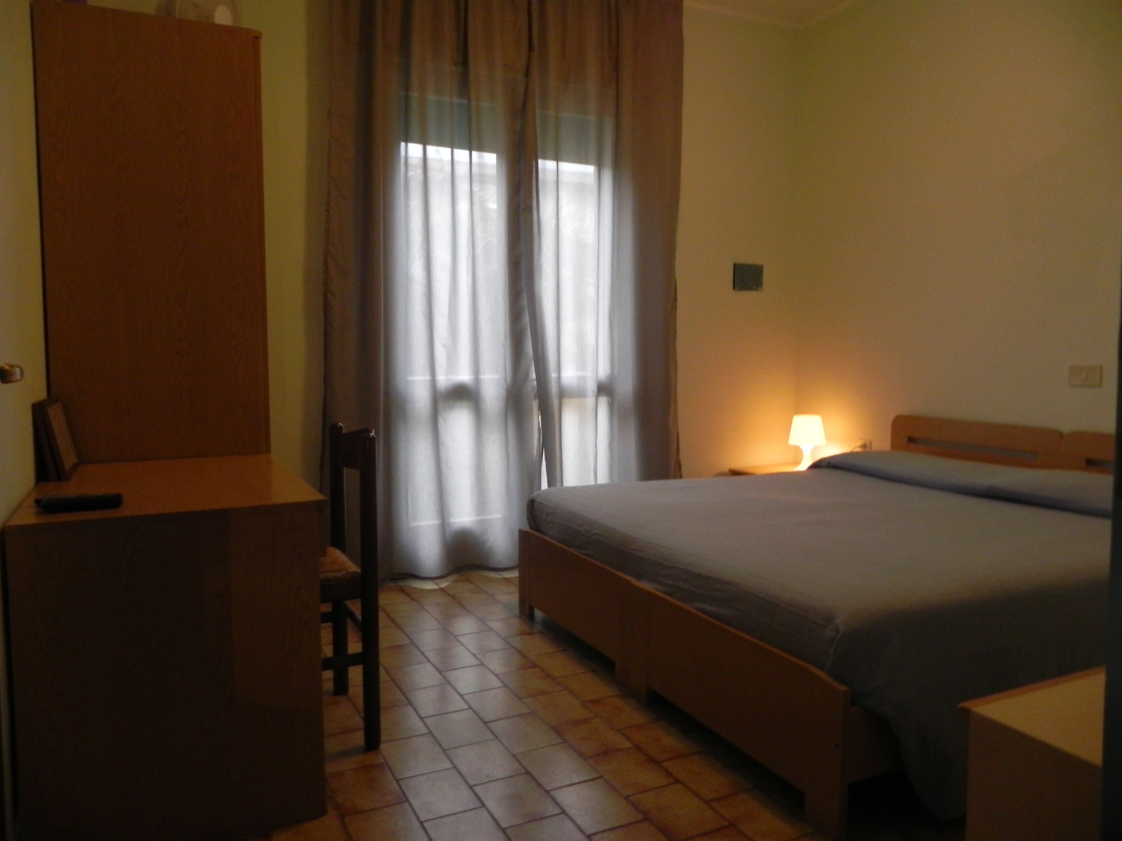 A hotel room with a bed, a desk, a chair, and a window with curtains.