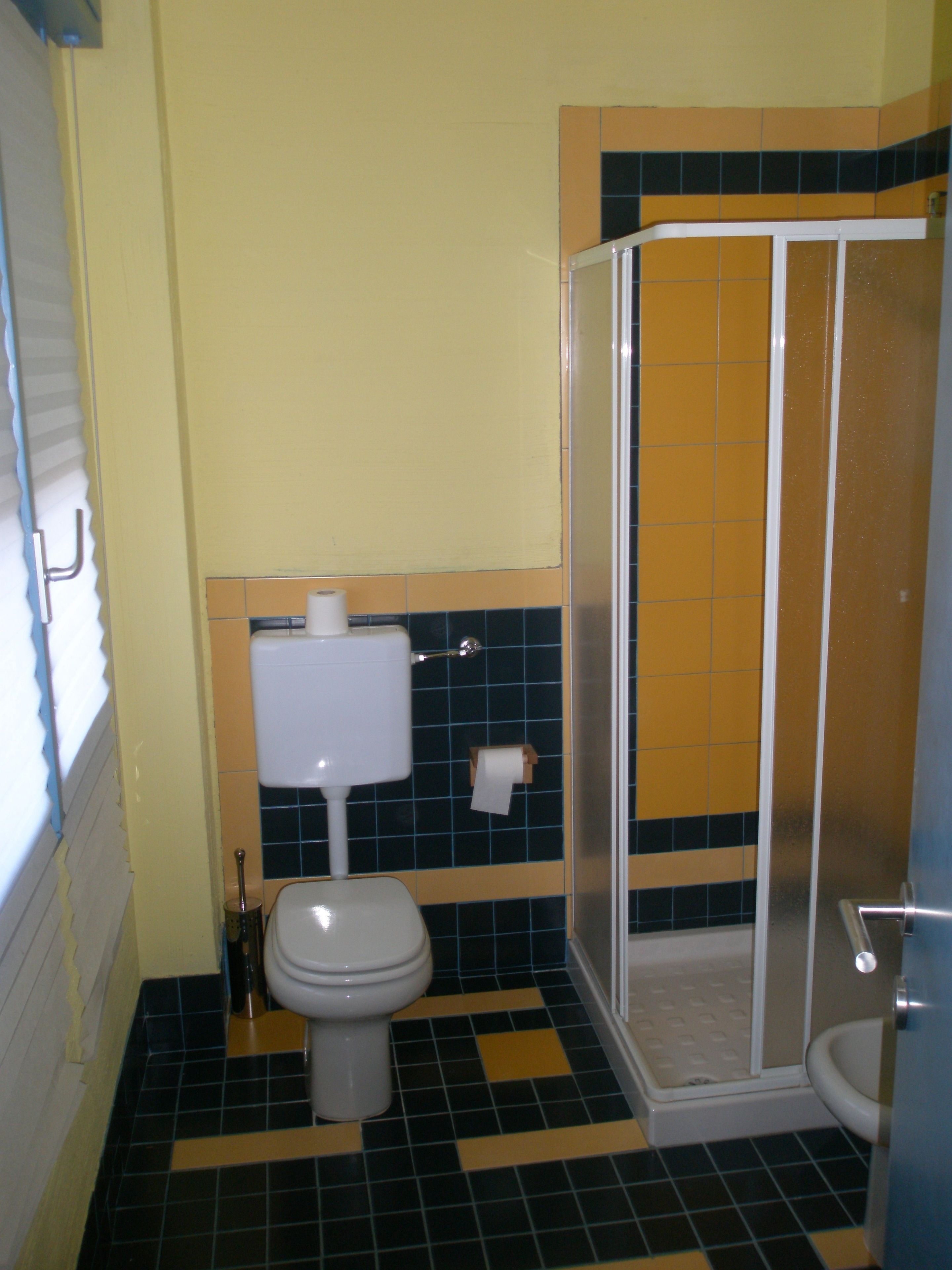 A bathroom with a toilet, a shower enclosure, and a tiled floor.