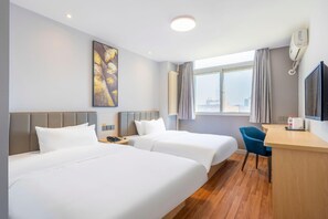 Ein Hotelzimmer mit zwei Betten, einem Schreibtisch, einem Stuhl, einem Fernseher, einem Gemälde und einem Fenster mit Vorhängen.
